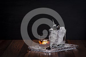 Front view of a glass of whiskey on a wooden table served on a crystal tray and an ice bucket with a dispenser