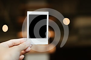 front view. hand of young woman holding blank Polaroid film. have blur interior cafe are background. image for abstract,body part