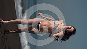 Front view of happy brunette woman in bikini running on black sandy beach of Pacific Ocean