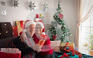 Front view of an happy couple of senior people wearing Santa`s hats and looking at camera. A lot of Christmas presents near to