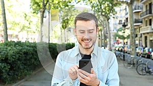 Front view of happy man using phone in the street
