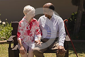 Front view of senior couple sitting on bench and looking each other in garden