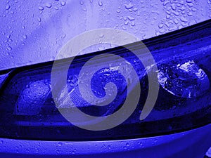 Front view of Headlight classic blue color covered with raindrops. Car exterior details of modern sport car