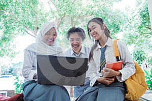 front view of high school students standing with a laptop computer, carrying books, and wearing a bag