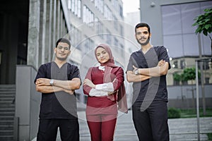 Three young confident multiethnic doctors, standing outside the hospital and looking at camera