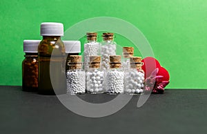 Front view of homeopath medicine bottles with flower buds and heart on green and dark background photo