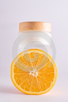 front view of a jar of vitamin C face cream on an orange, the presence of sliced citrus fruits symbolizes the presence