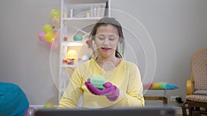 Front view joyful woman waving at laptop pouring detergent on sponge talking. Portrait of smiling confident Caucasian