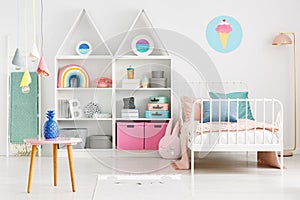 Front view of a kid`s room interior with a table, shelves with b