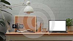 Front view of laptop computer with empty display, lamp, coffee cup and board on wooden desk