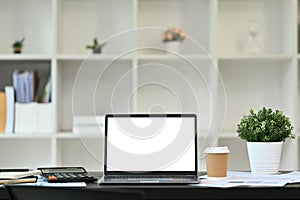 Front view laptop computer with empty screen, calculator and financial documents on office desk