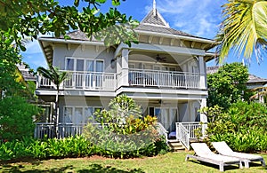 Front View of A large bungalow resort with sundeck chairs in front surrounded by green trees and plants