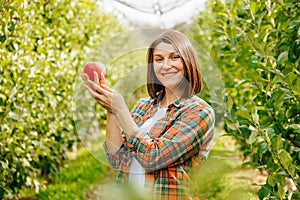 Front view looking at camera young woman farmer holding a ripe apple in her hands and smiling.