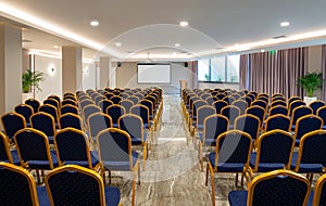 Front view of luxury auditorium interior with empty white screen. Modern conference hall with rows of vintage blue, golden chairs