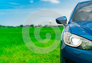 Front view of luxury blue compact SUV car with sport and modern design parked on green grass field with blue sky and white clouds