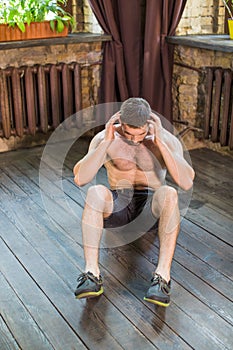 Front view of man doing sit ups and crunches on the floor at home.