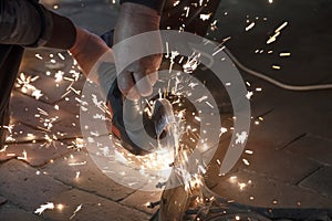 Front view of a man`s hands working on a metal part of a garden bench, using an electric grinder while sparks are flying around i