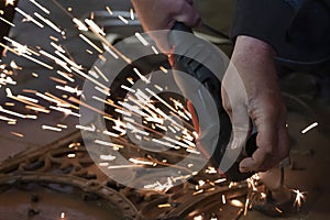 Front view of a man`s hands working on a metal part of a garden bench, using an electric grinder while sparks are flying around i