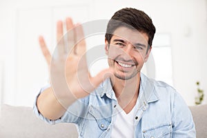 Front view on man showing greeting gesture to laptop camera starting video conference with friend or partner using video call chat