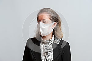 Front view of middle aged mixed race woman in formal wear wearing white surgical mask for protection against coronavirus COVID-19