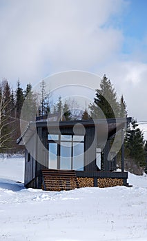 Front view of modern black wooden cabin with panoramic windows in winter