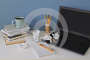 Front view on modern creative workspace of a creative entrepreneur with mess on the office table with crumpled paper, blue cup of