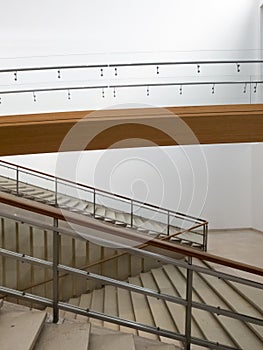 Front view of modern marble stairs, wooden railing and white walls. Nobody inside