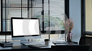 Front view of modern workspace with white screen computer, coffee cup and paperwork on black table.