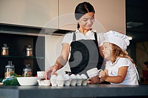 Front view. Mother with her daughter are preparing food on the kitchen