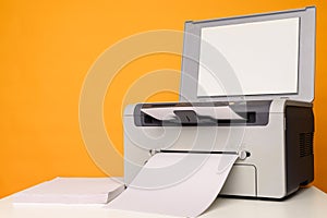 Front view of a multifunction device - printer, copier, scanner and a blank sheet of A4 paper on a white table