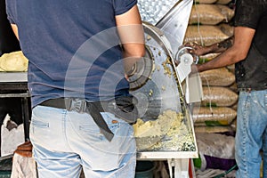 Front view of a nixtamal mill while a man takes out the dough that is being produced