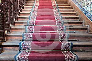 Front view of old ascending wooden stairs with ornate red carpet