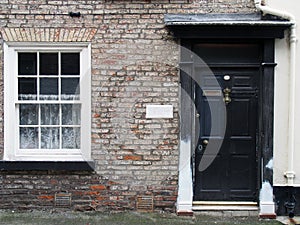 front view of a old small english terraced brick house with black painted door and white window