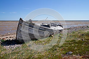 Front view of old wooden boat wrecked and stranded on a rocky shoreline