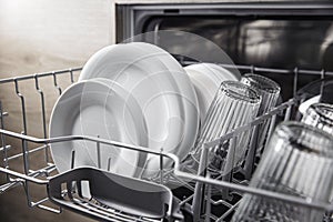 Open dishwasher with clean utensil inside, cutlery, glasses, dishes at kitchen