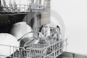 Open dishwasher with clean utensil inside, cutlery, glasses, dishes at kitchen