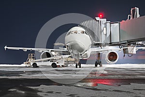 Front view of the passenger aircraft stands at the jetway on night airport apron. The baggage compartment of the airplane is open