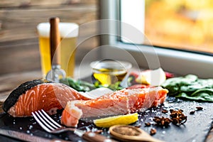 Front view of pieces of raw salmon fillet preparing for cooking on cutting board with glass of beer