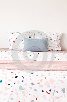 Front view of a pink blanket on a bed, two patterned pillows and photo