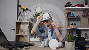 Front view of pleasant modern teen boy in virtual reality headset which playing video game at home