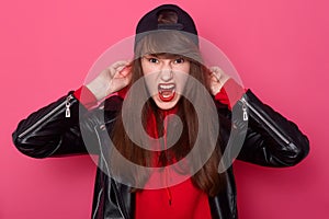 Front view portrait of angry girl with long hair and makeup in casual style black leather jacket standing and screaming in studio