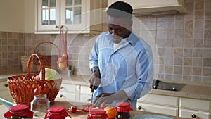 Front view portrait of confident young man cutting ingredients for healthful organic vegan salad singing. African