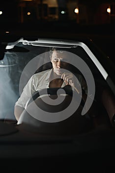 Front view. Portrait of a handsome man driving his car at night. The traffic lights behind him