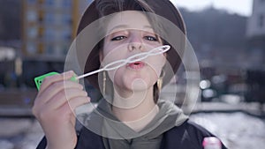 Front view portrait of relaxed beautiful woman blowing soap bubbles in slow motion and looking at camera. Close-up of