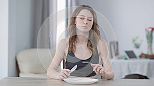 Front view portrait of slim charming young Caucasian woman cutting cucumber slice eating healthful organic vegetable
