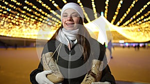 Front view portrait of smiling happy young woman posing with ice skates at Christmas ice rink. Positive Caucasian