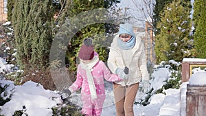 Front view portrait of smiling satisfied grandmother and granddaughter walking on sunny winter day holding hands. Happy
