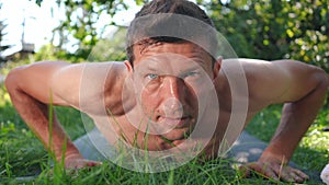 Front view portrait of sweating concentrated sportsman moving down doing push-ups looking at camera. Perspiring