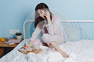 Portrait of thoughtful serious confident brunette friendly smart girl sitting on bed talking on phone, drinking coffe photo