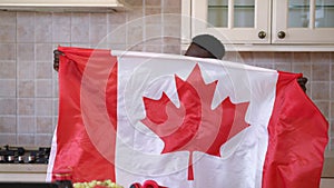 Front view positive African American man shacking Canadian flag posing in kitchen indoors. Portrait of happy confident